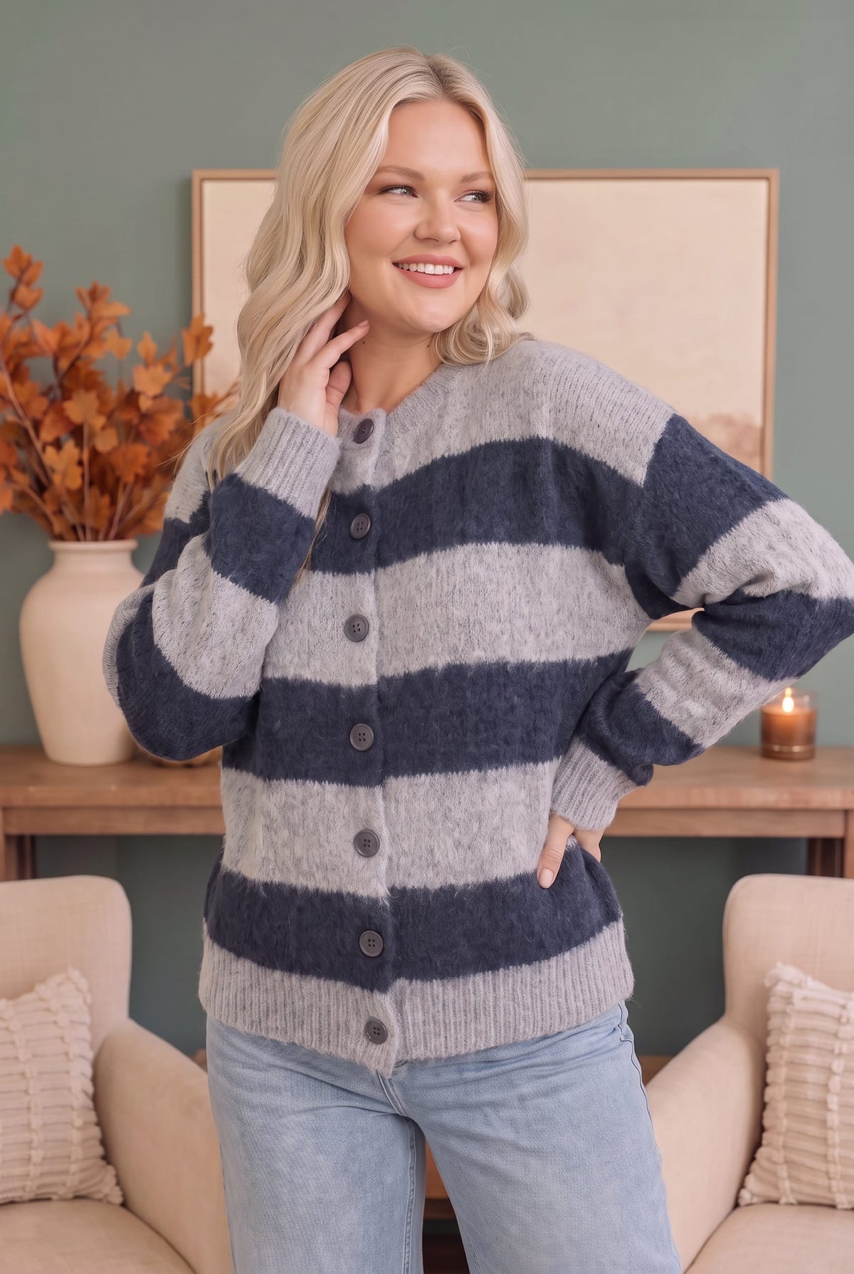 A woman wearing a fuzzy knit cardigan sweater with horizontal navy and light gray stripes, paired with light blue jeans, standing in a cozy living room setting.
