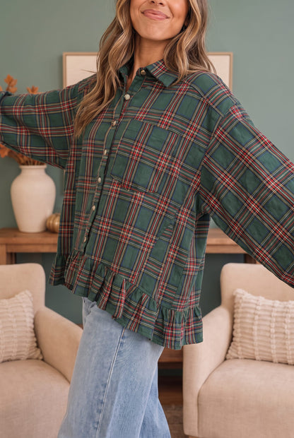A woman wearing a green plaid button-up shirt with a ruffled hem and light blue jeans, standing in a living room setting with beige armchairs and a green wall.