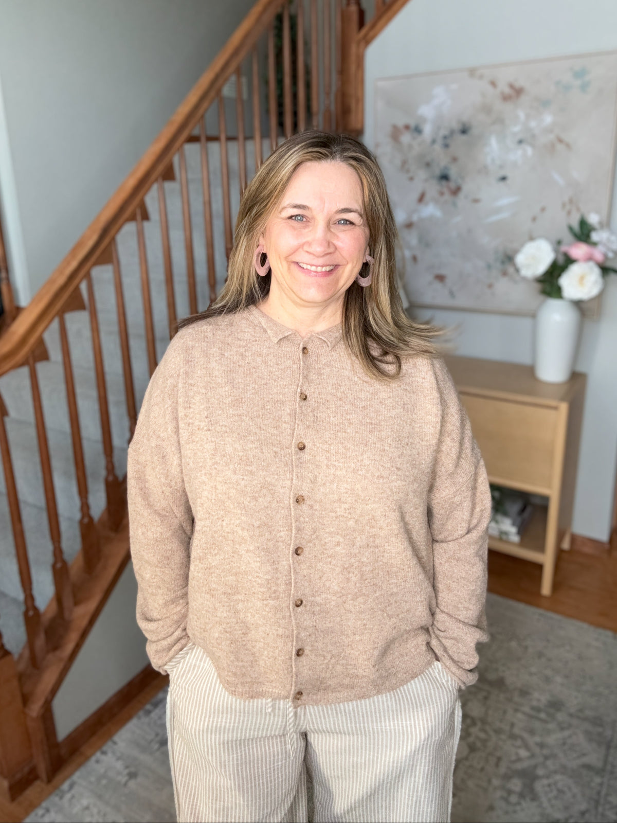 Woman standing in a home interior with wooden staircase and decor.