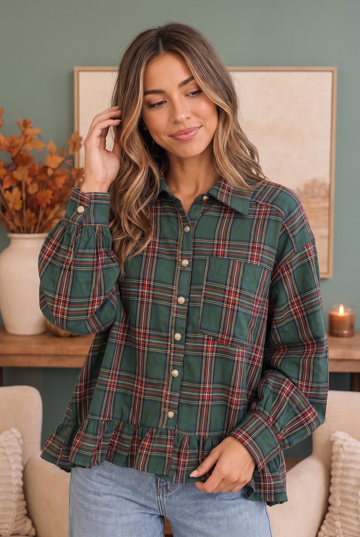 A woman wearing a green plaid button-up shirt with red and white stripes, paired with light blue jeans, standing in a cozy room setting.