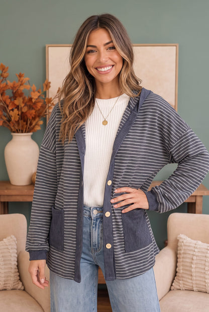 A woman modeling a navy blue and white striped cardigan with a ribbed knit collar, cuffs, and hem, worn over a white ribbed top and light blue jeans in a cozy indoor setting.