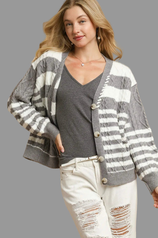 Woman wearing a gray and white striped cardigan over a gray shirt with white pants on a beige background