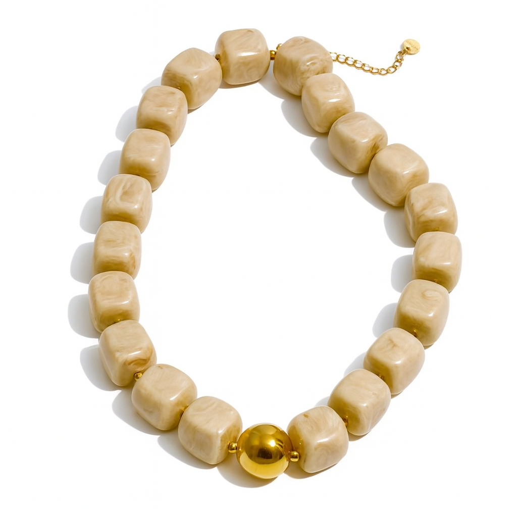 A chunky beaded necklace made of rounded, polished light beige stone beads with a single shiny gold ball bead and gold chain extender, displayed on a clean white background.
