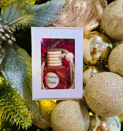 Small bottle of cinnamon vanilla scented car diffuser in a decorative box surrounded by gold Christmas ornaments.