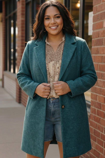 Woman wearing a teal coat standing against a brick wall.