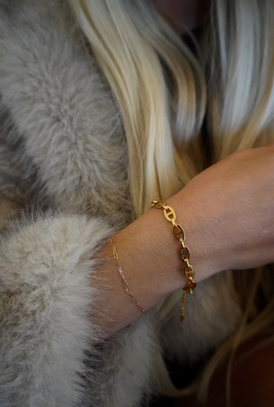 Close-up of a person wearing gold bracelets on a soft textured background