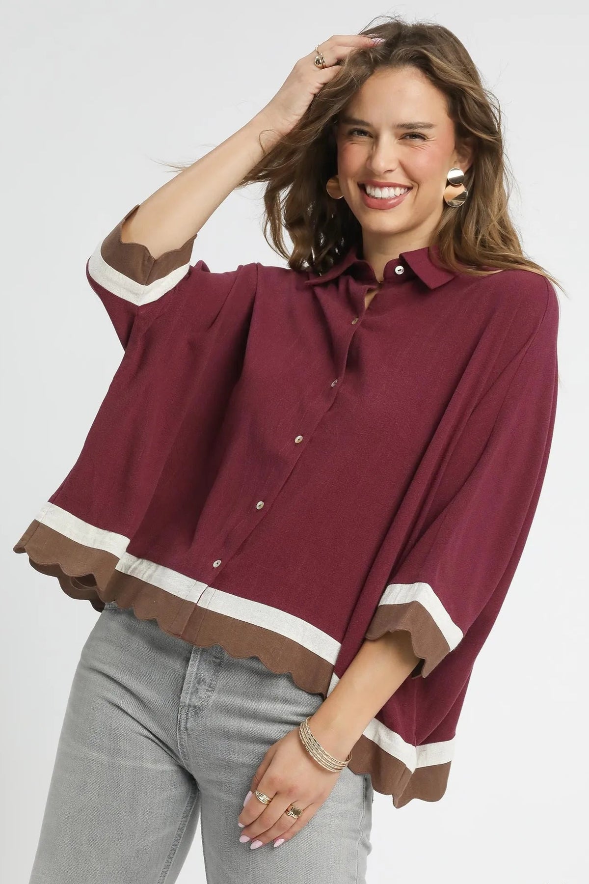 Woman wearing a maroon blouse with white trim on a plain background