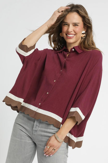 Woman wearing a maroon blouse with white trim on a plain background