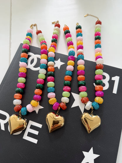 Three colorful beaded necklaces with gold heart pendants, displayed on a black printed card.