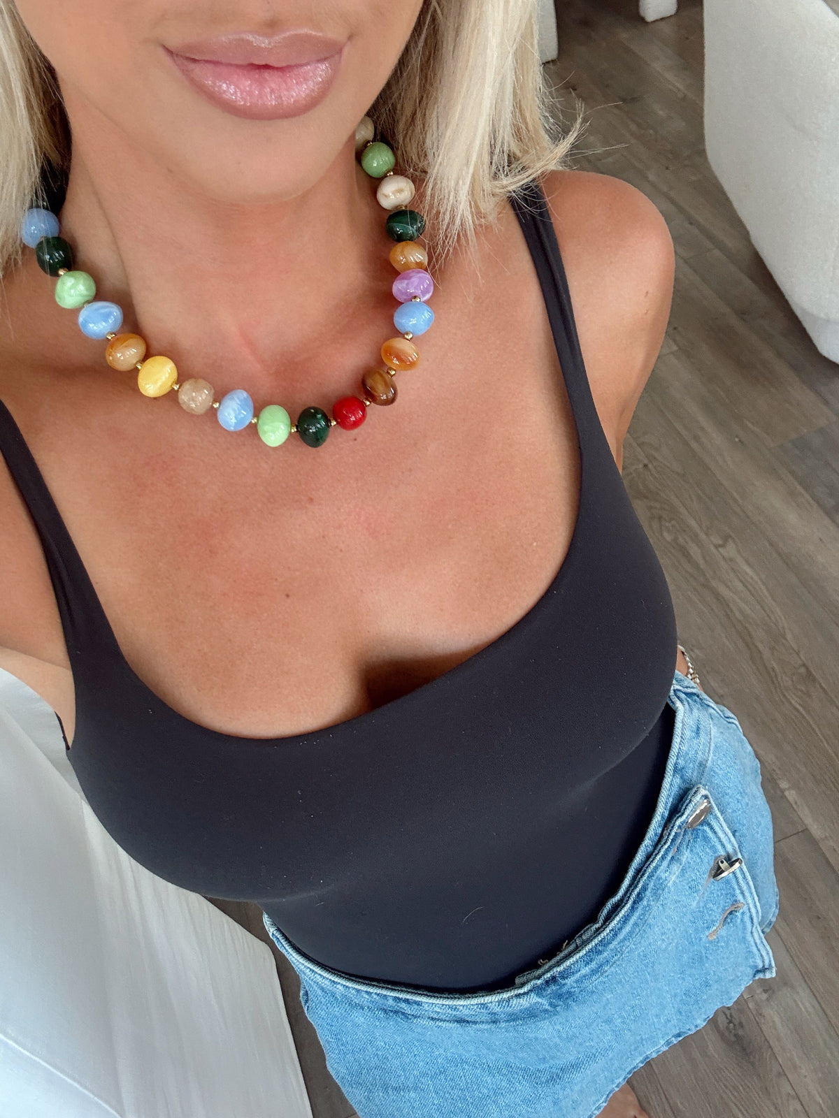 A close-up lifestyle shot of a woman wearing a colorful beaded necklace with a black camisole top and denim shorts.