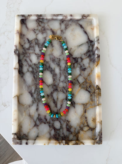 A colorful beaded necklace with a gold clasp, displayed on a rectangular white and gray marble tray.