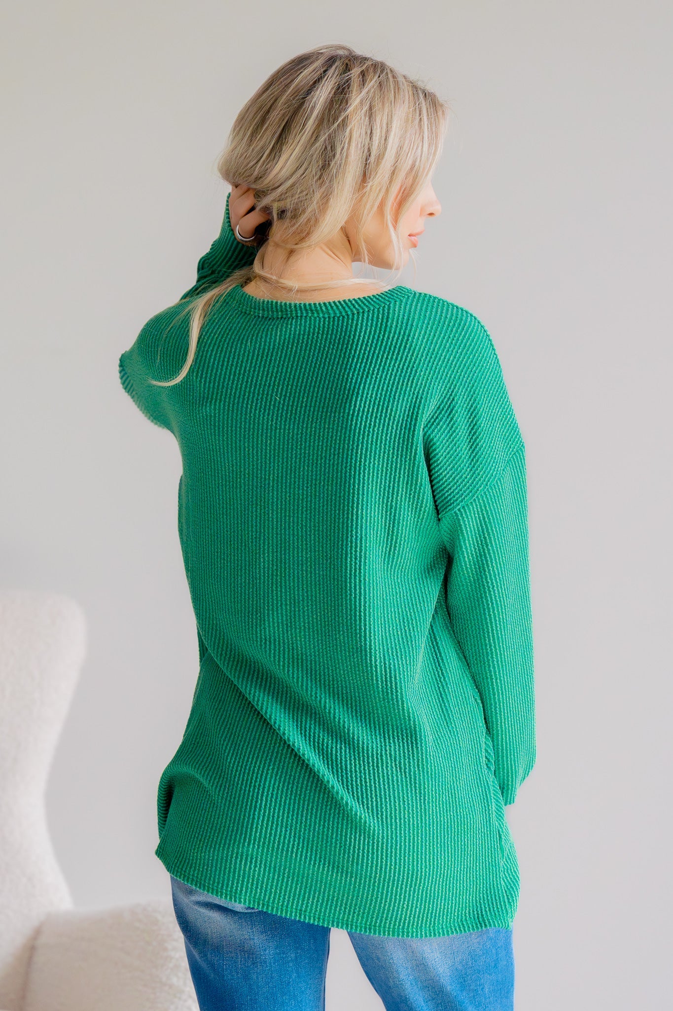 Person wearing a green sweater and blue jeans against a white background