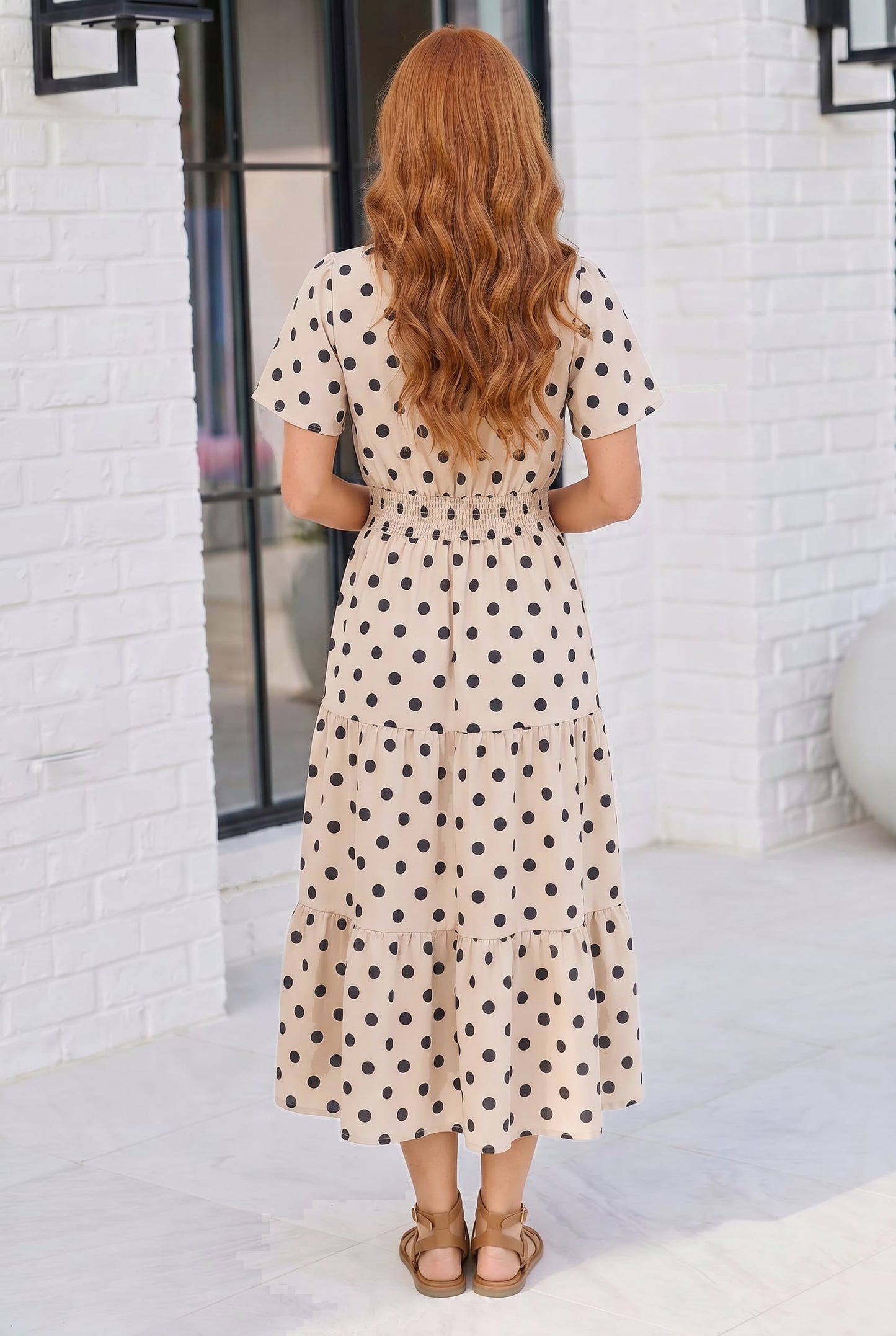 Woman wearing a polka dot dress standing in front of a white brick wall.