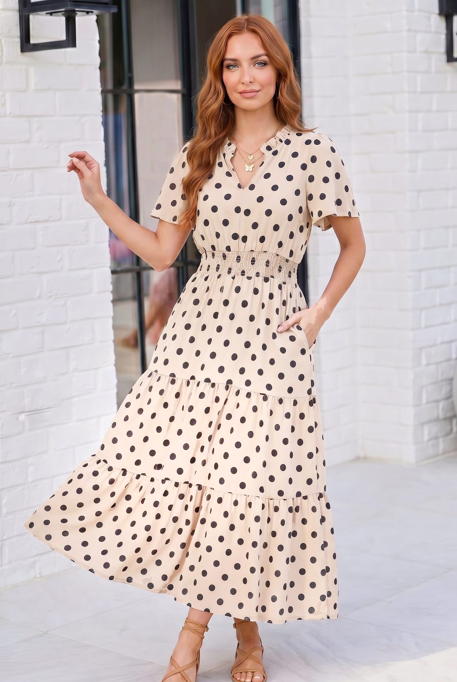 Woman wearing a polka dot dress standing against a white brick wall.