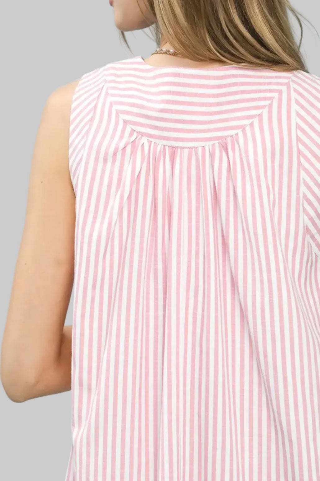 Close-up of a person wearing a pink and white striped sleeveless top against a light blue background.