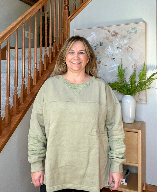Woman wearing a light green sweater standing in a home setting with a staircase and decorative elements.