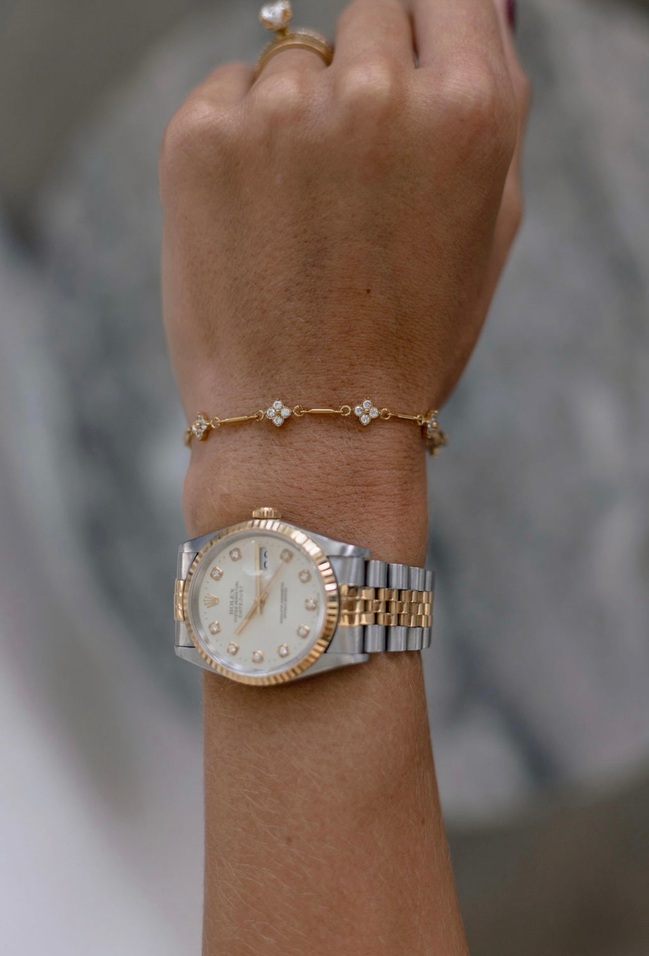 A close-up of a person's wrist wearing a two-tone Rolex Lady Datejust watch with a white dial and bezel, along with a delicate gold bracelet and ring.