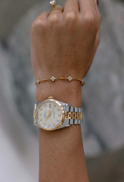 A close-up of a person's wrist wearing a two-tone Rolex Lady Datejust watch with a white dial and bezel, along with a delicate gold bracelet and ring.