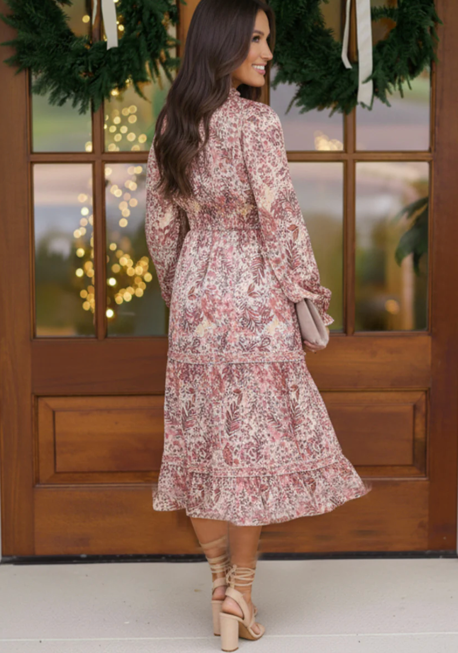 Woman in a floral dress standing in front of a wooden door with wreaths and lights.