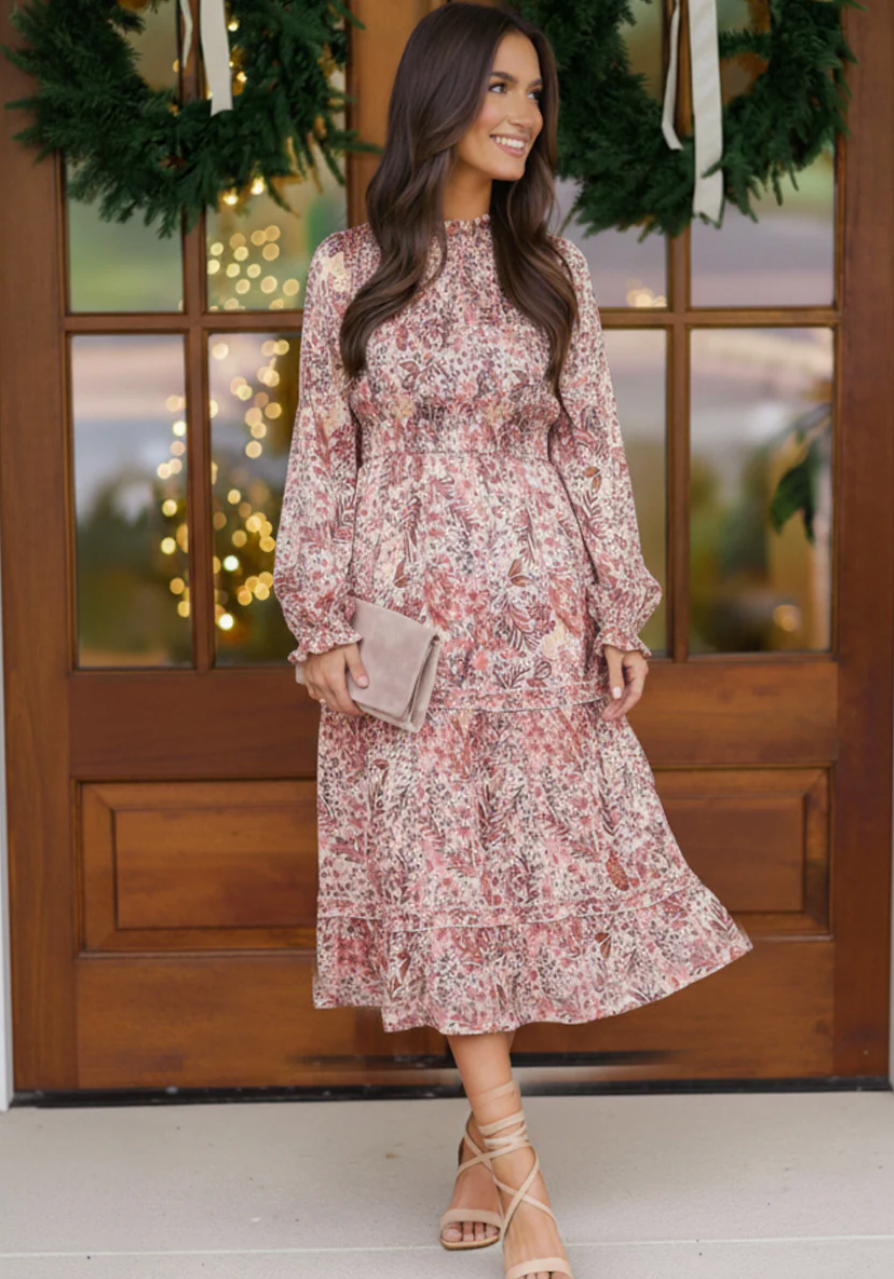 Woman in a floral dress standing in front of a wooden door with decorative lights.