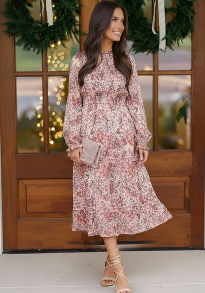 Woman in a floral dress standing in front of a wooden door with decorative lights.