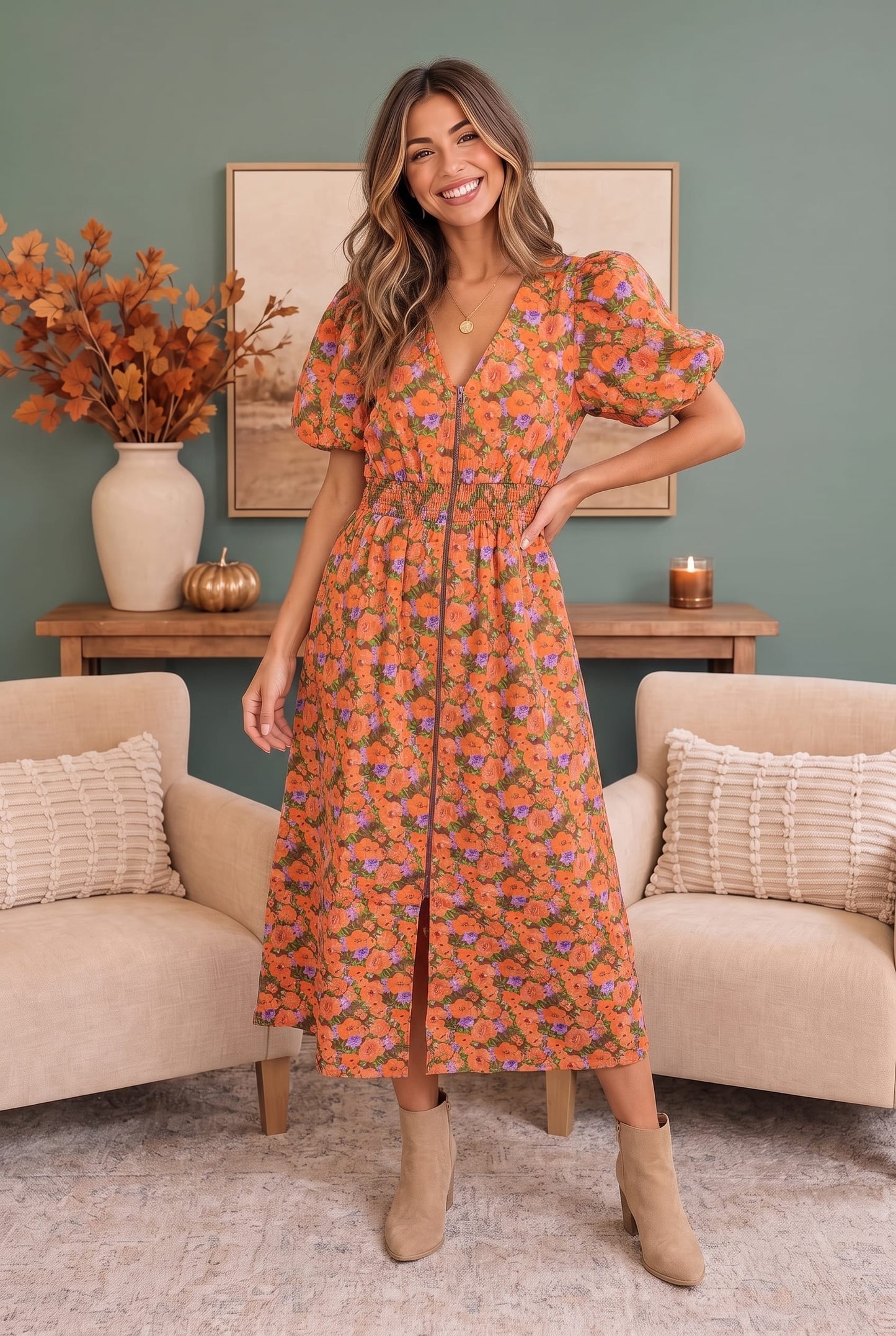 A woman modeling a short-sleeve orange midi dress with a colorful floral pattern, standing in a cozy living room setting with beige armchairs and a green wall.