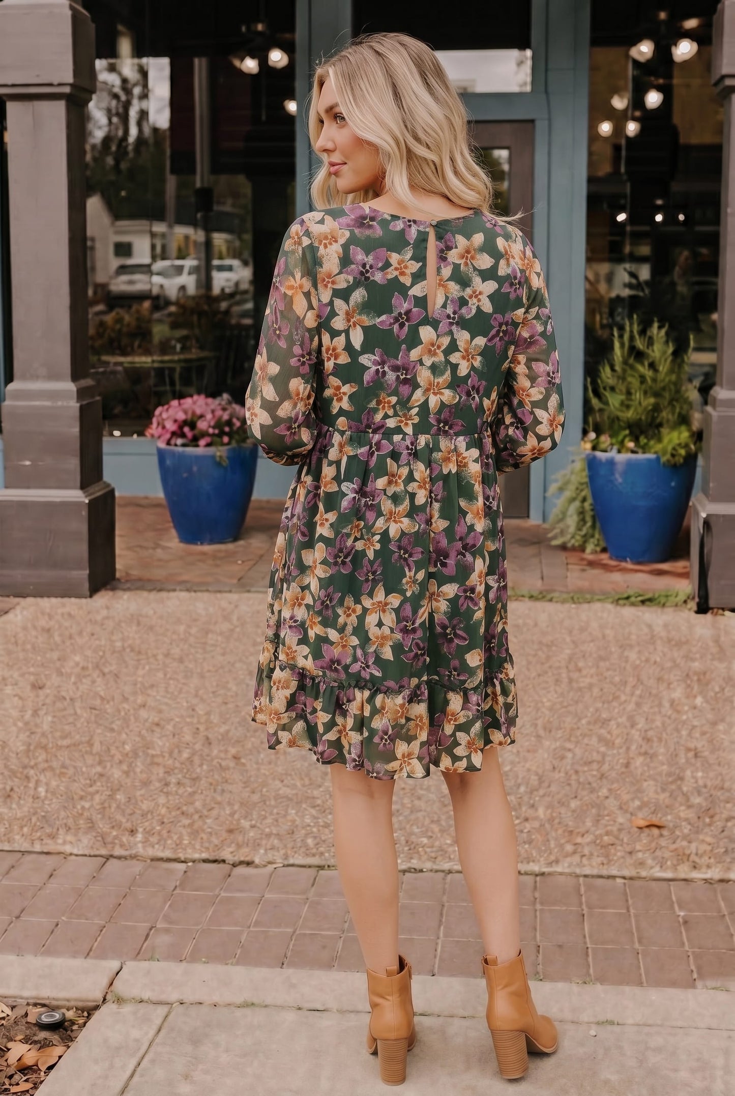 Woman wearing a floral dress standing on a sidewalk with storefronts in the background