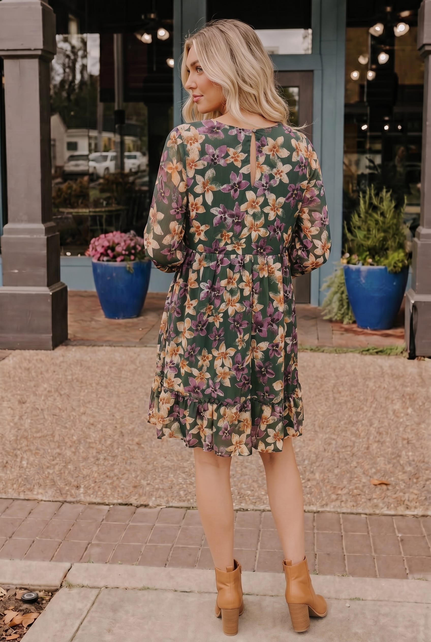 Woman wearing a floral dress standing on a sidewalk with storefronts in the background