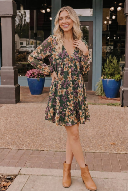 Woman in a floral dress standing on a sidewalk with storefronts in the background