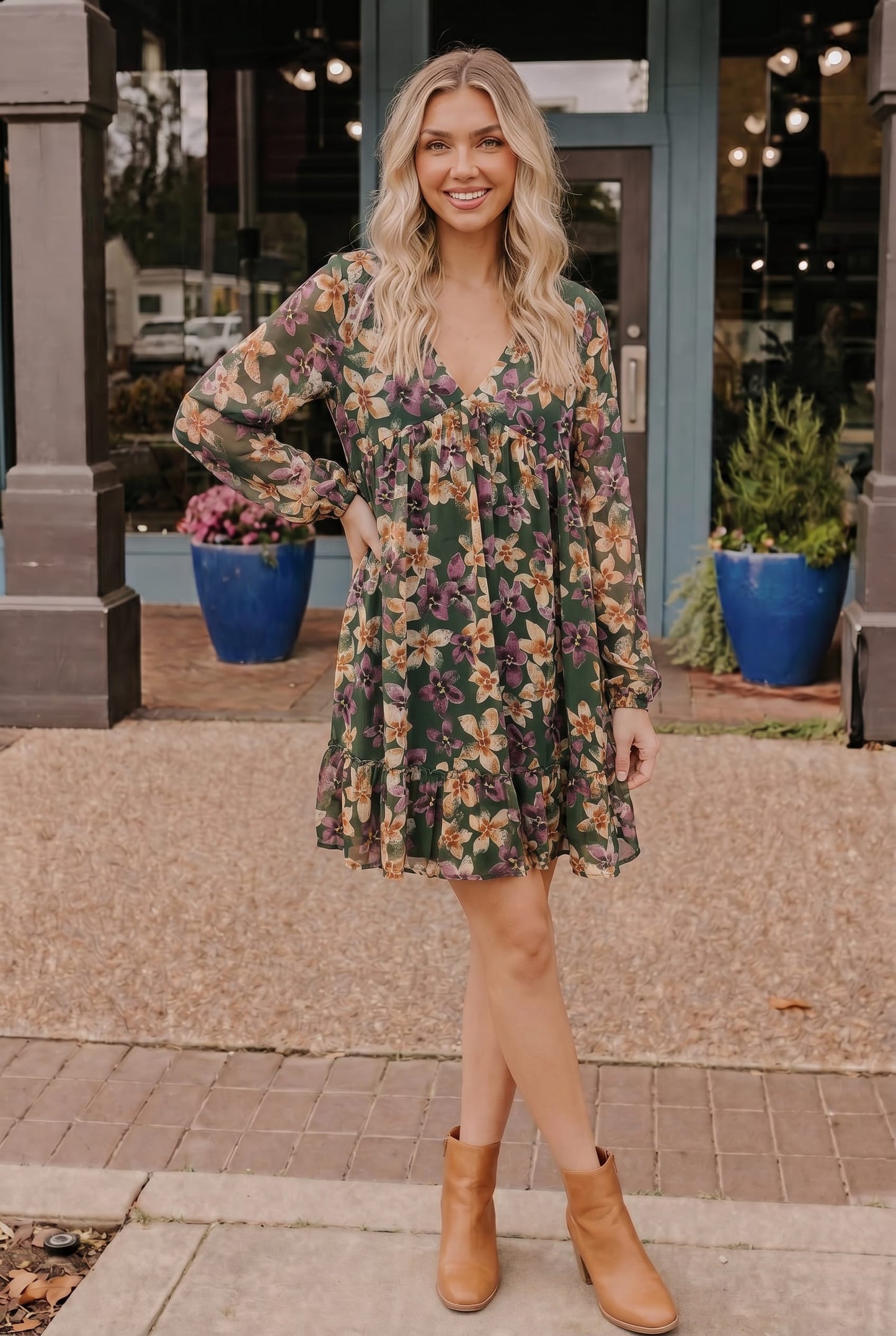 Woman wearing a floral dress with long sleeves and brown boots standing on a sidewalk.