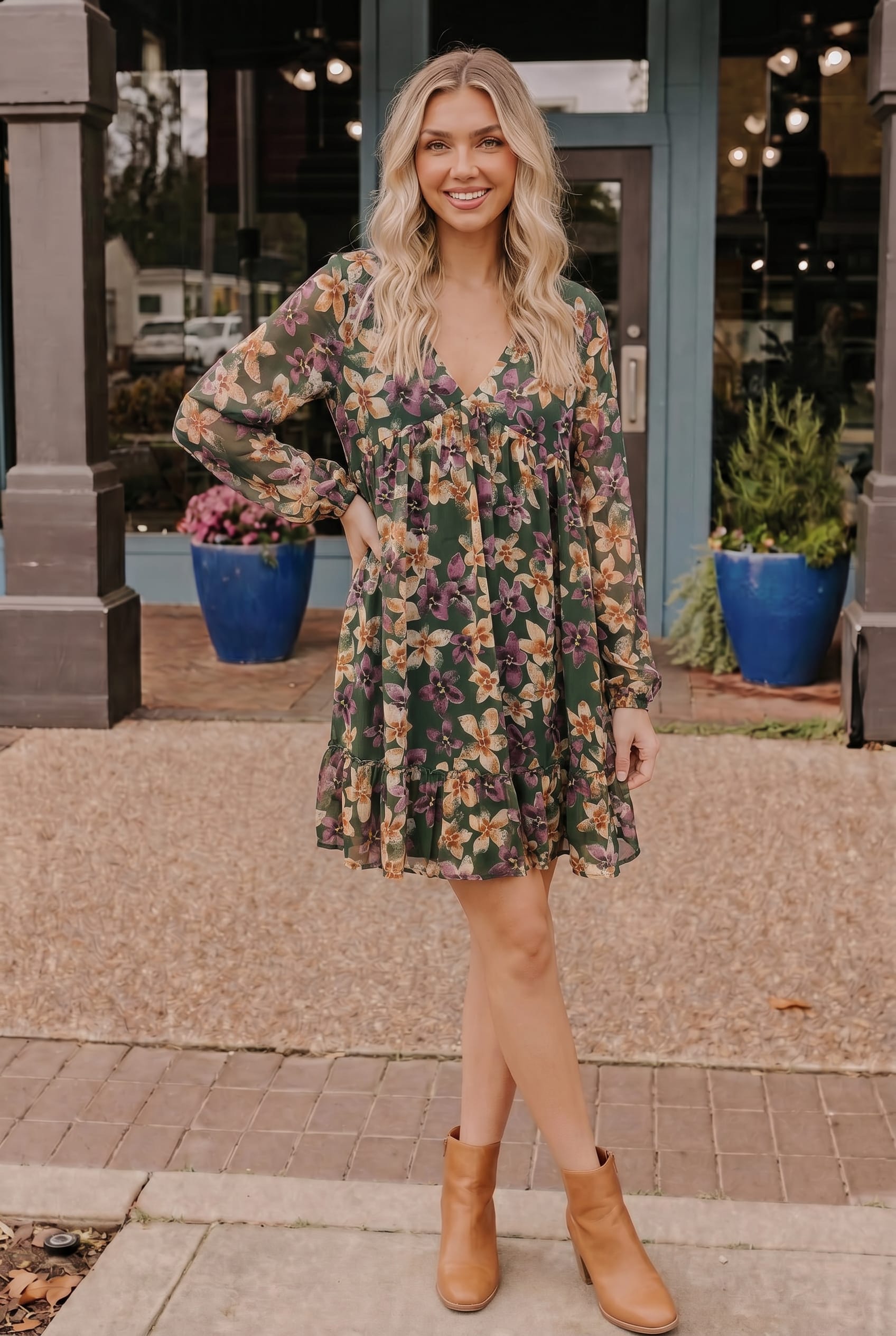 Woman wearing a floral dress with long sleeves and brown boots standing on a sidewalk.