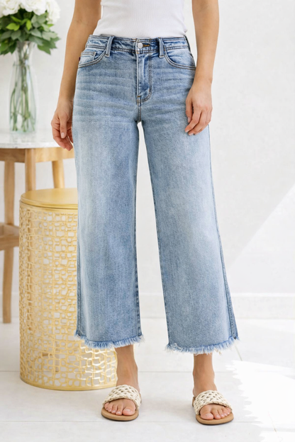 Person wearing light blue jeans standing in a room with a white wall and a woven stool.