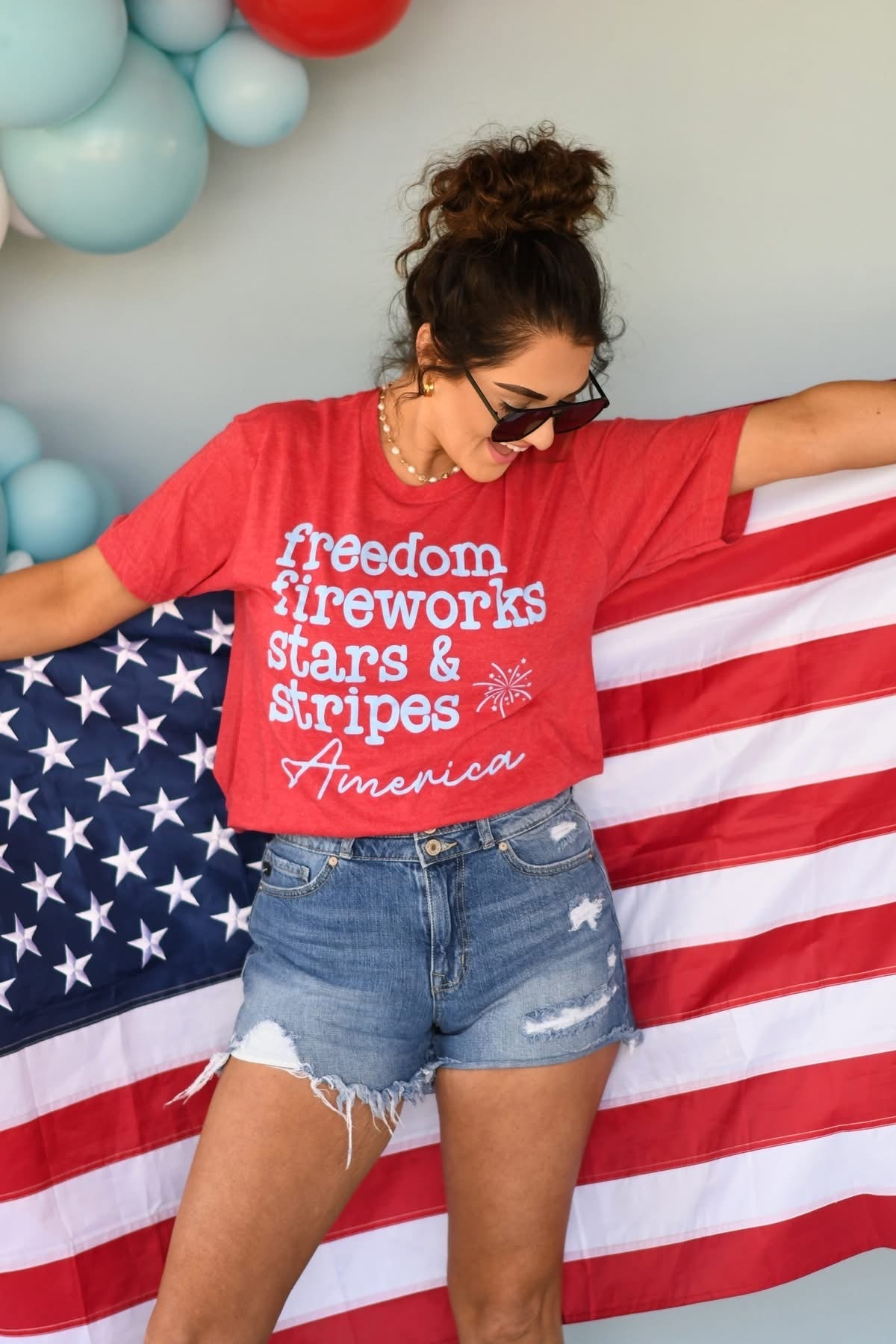 Woman wearing a red t-shirt with patriotic text, standing next to an American flag.