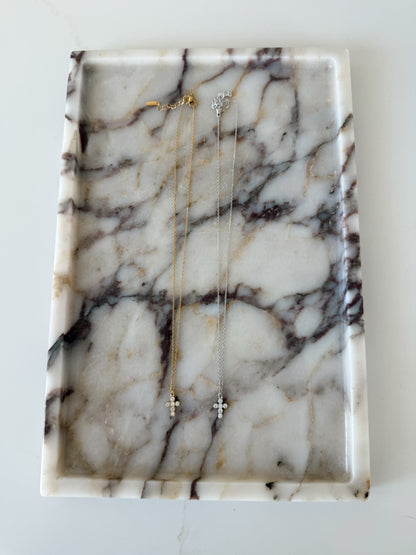 Two delicate cross pendant necklaces, one gold and one silver, displayed on a white marble jewelry tray with dark veining.