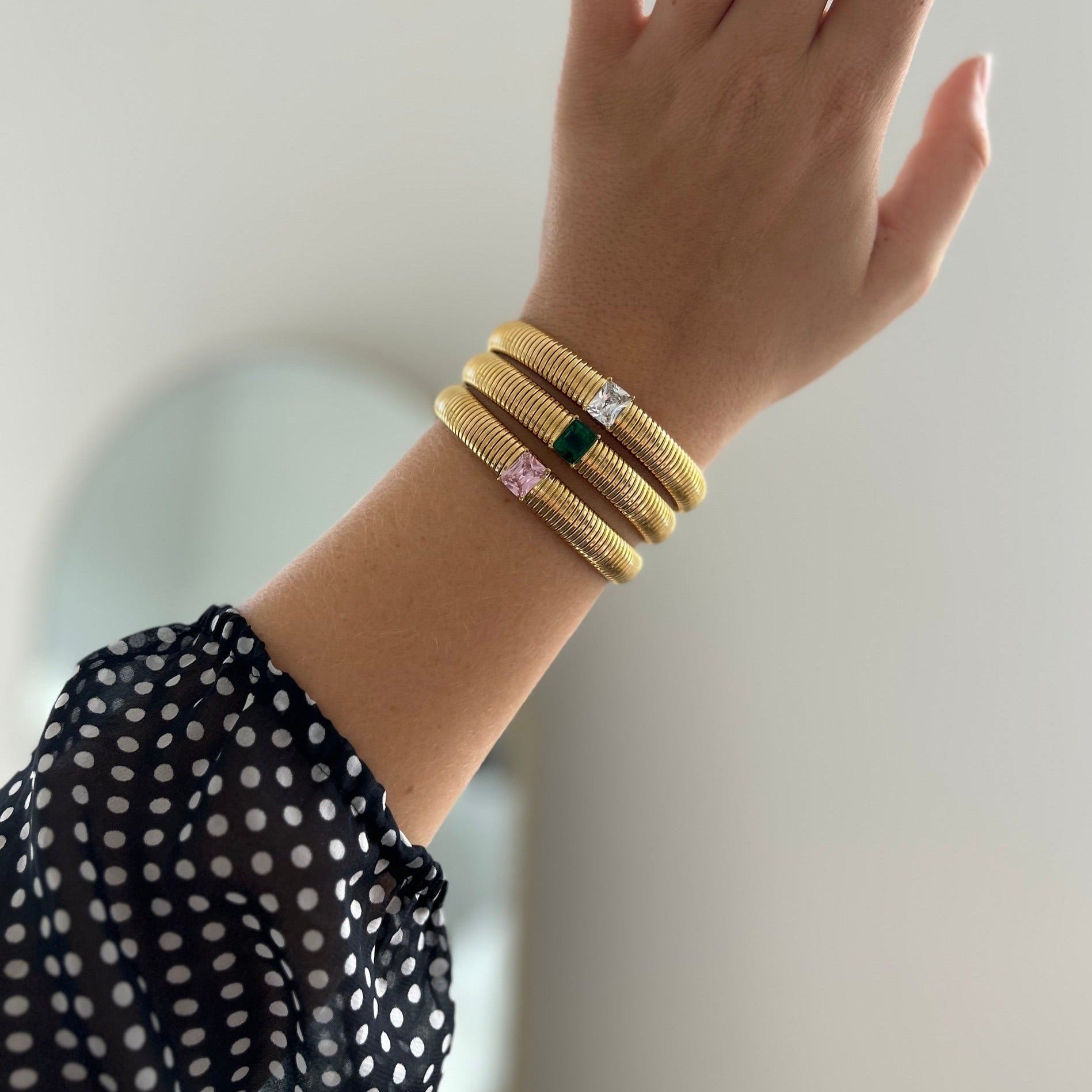 Hand wearing gold bracelets with gemstones on a neutral background