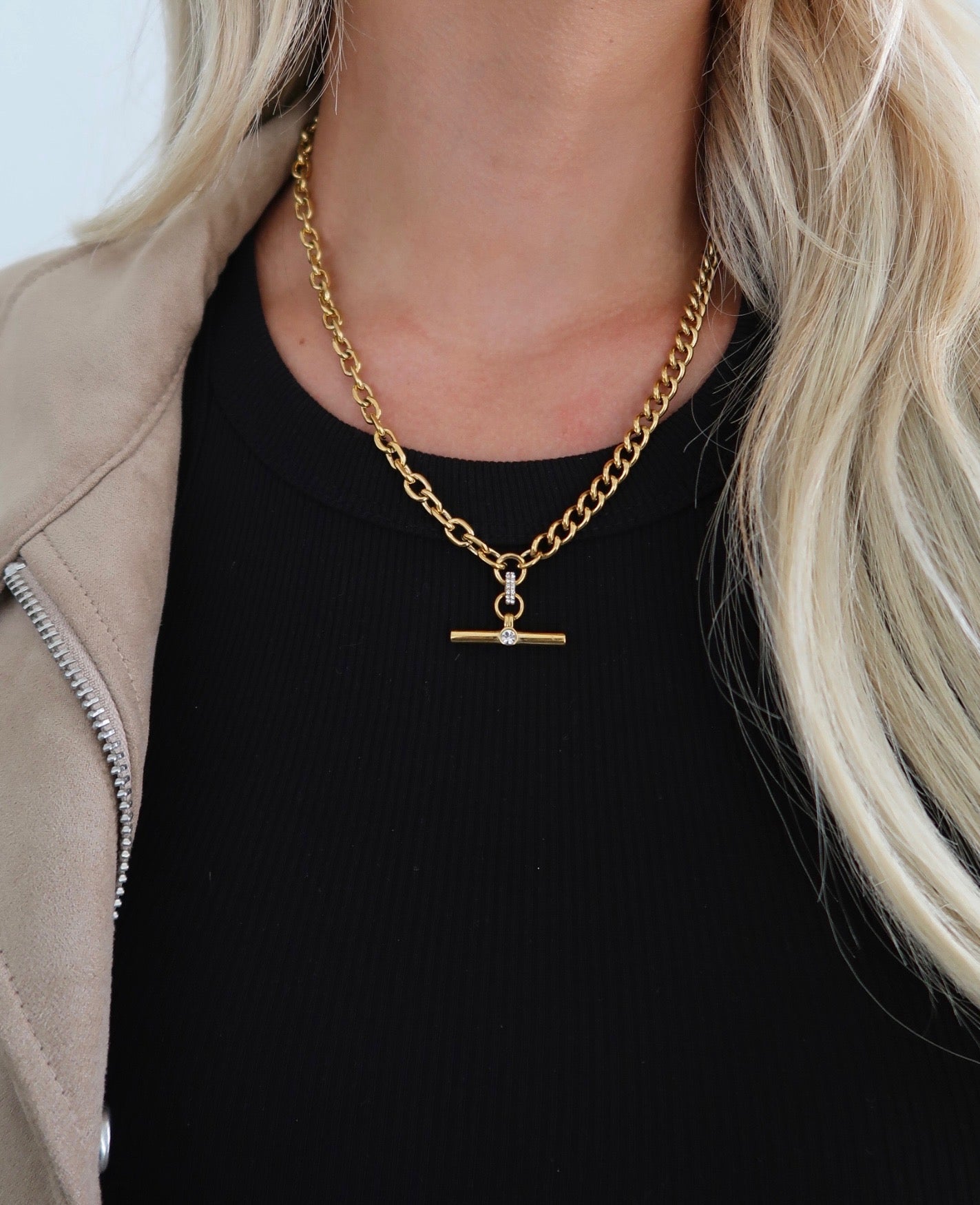 Gold chain necklace with a pendant worn by a person with blonde hair.