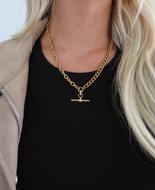 Gold chain necklace with a pendant worn by a person with blonde hair.