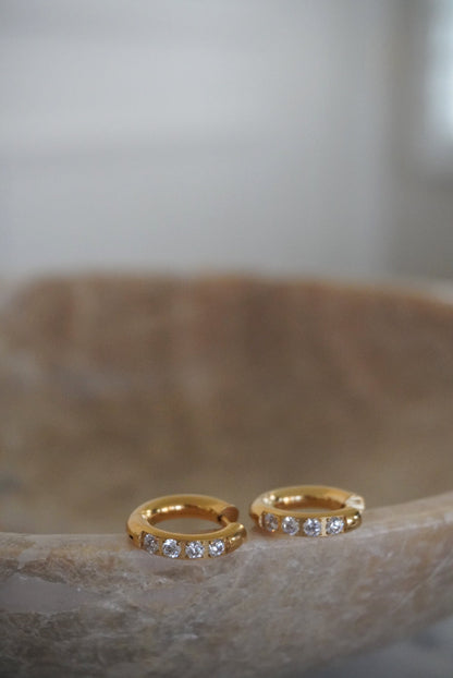 Gold hoop earrings with embedded stones on a stone surface