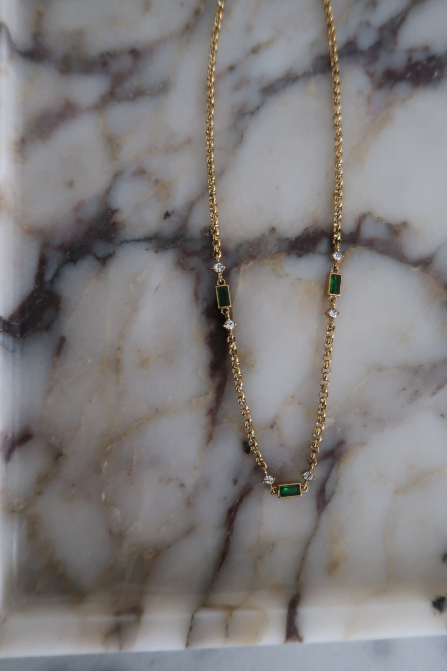 Gold necklace with green gemstones on a marble surface