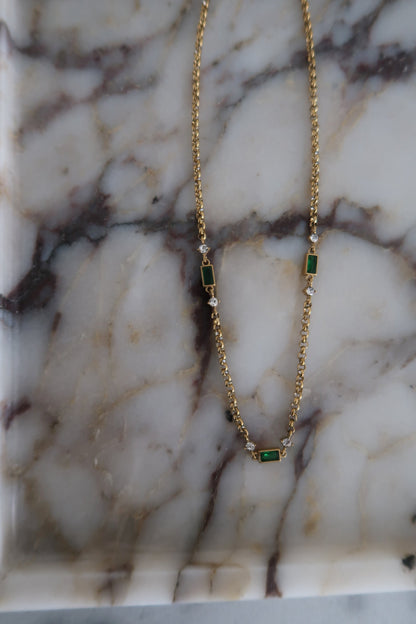 Gold necklace with green gemstones on a marble surface