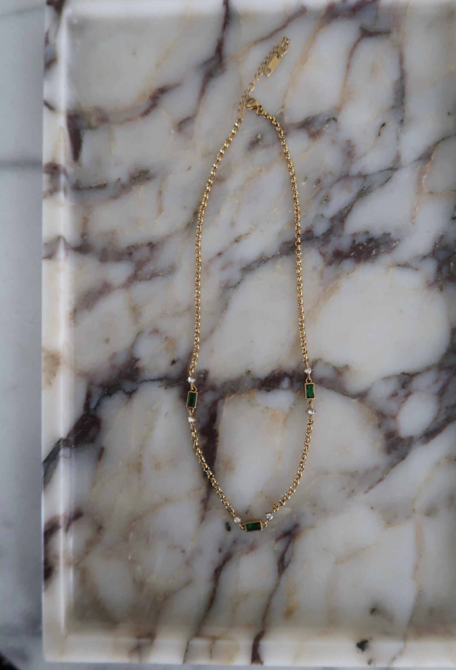 Gold necklace with green gemstones on a marble surface