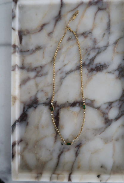 Gold necklace with green gemstones on a marble surface
