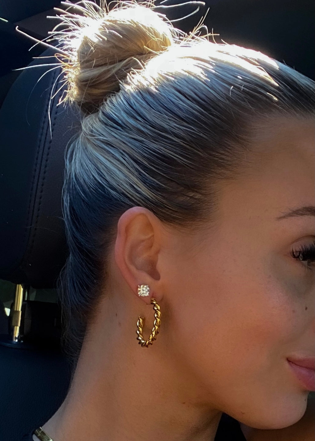 Close-up of a person wearing gold hoop earrings with a blurred background