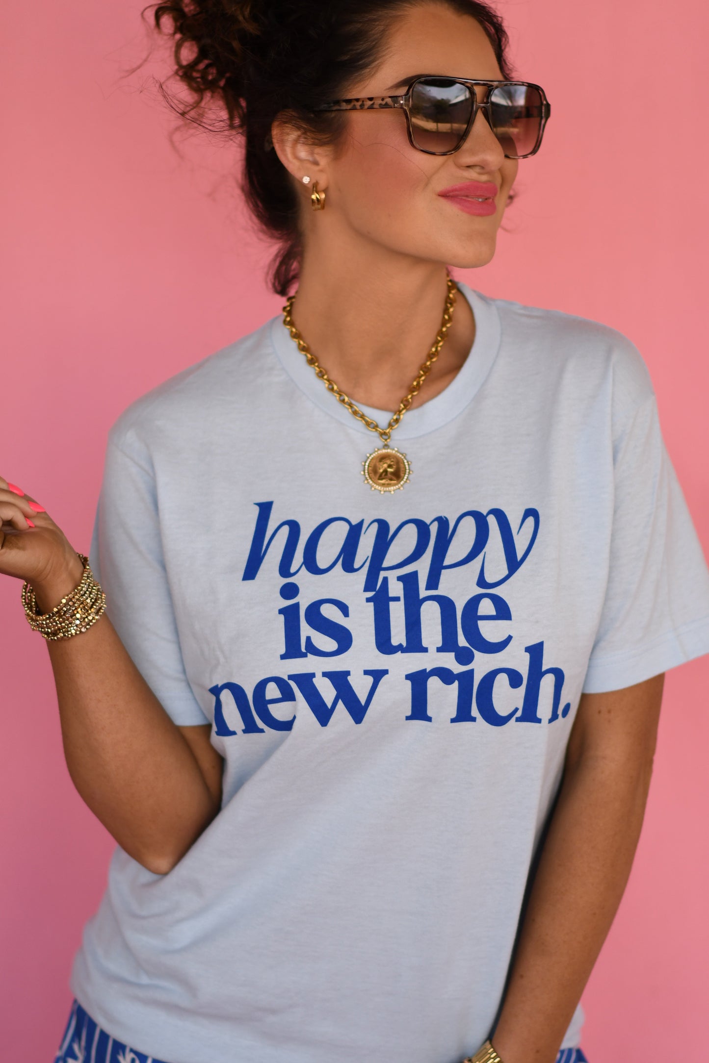 Woman wearing a t-shirt with 'happy is the new rich' text against a pink background