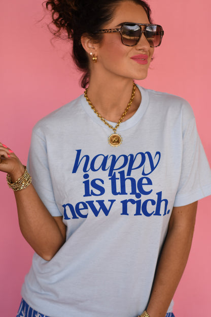 Woman wearing a t-shirt with 'happy is the new rich' text against a pink background