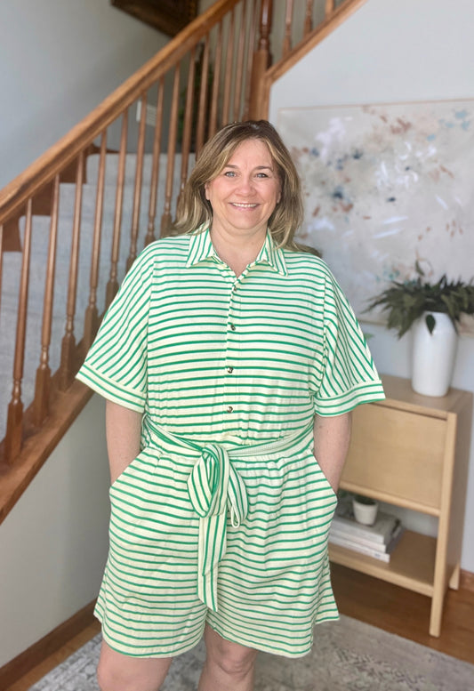 Woman wearing a green and white striped dress standing in a home setting with a staircase.