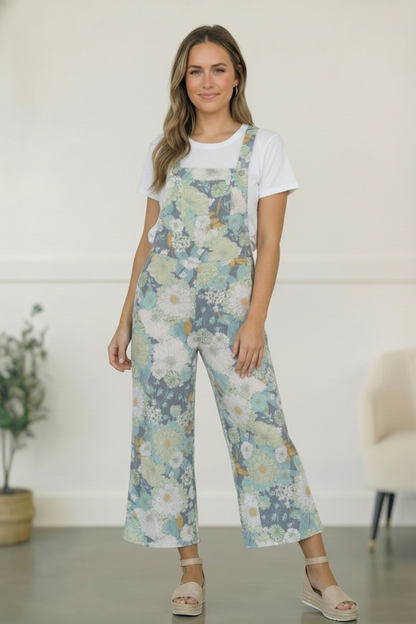 Woman wearing floral overalls and a white shirt indoors.