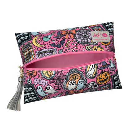 A rectangular zippered pouch with a pink and black Halloween-themed pattern featuring ghosts, pumpkins, skulls, and spiders. The pouch has a silver tassel zipper pull and a small brand label on the upper right.
