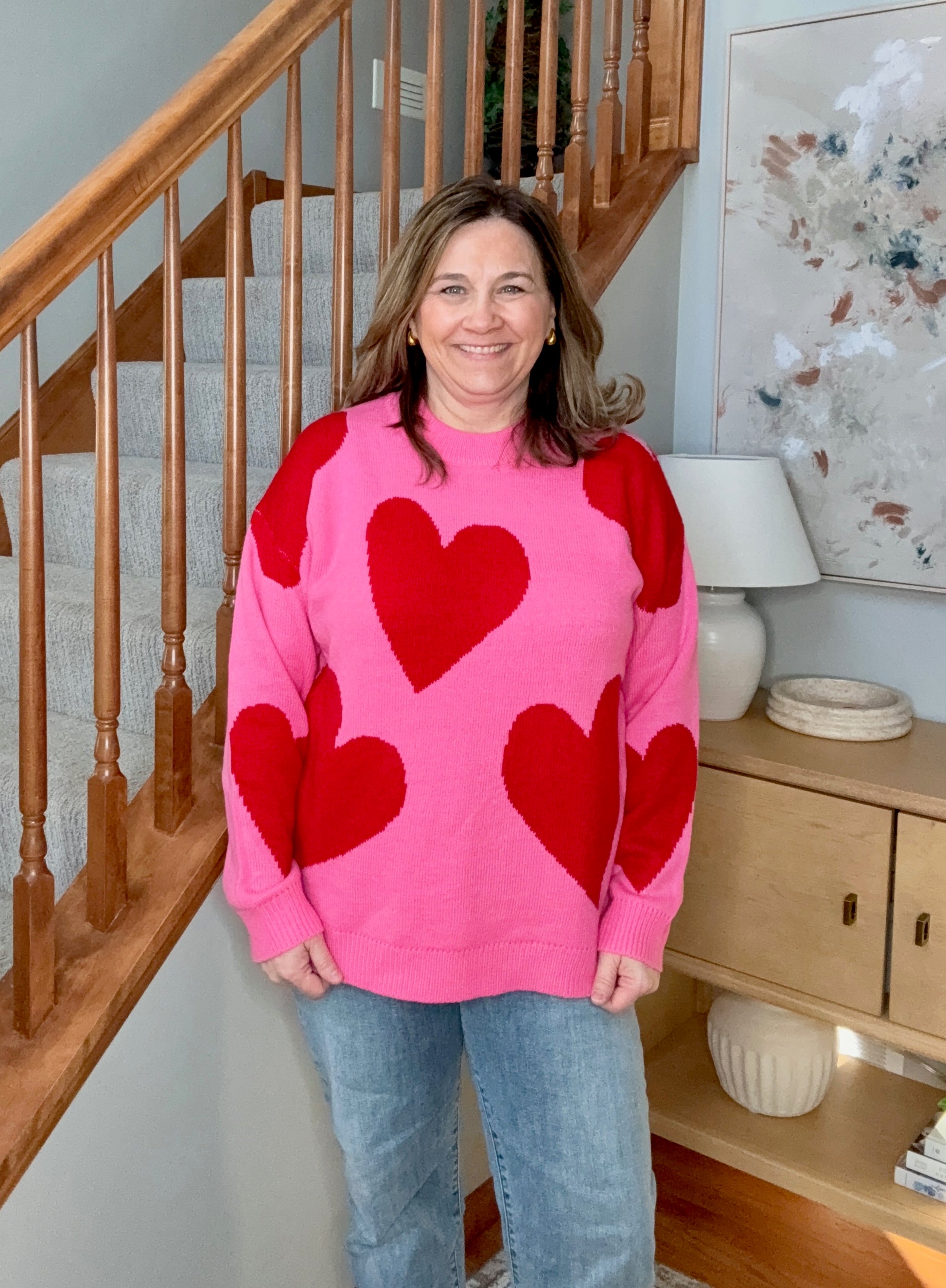 Woman wearing a pink sweater with red hearts standing in a home setting.