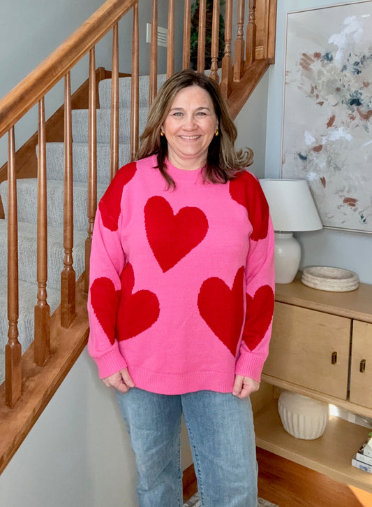 Woman wearing a pink sweater with red hearts standing in a home setting.